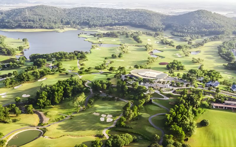 Aerial view of Chi Linh Star Golf & Country Club in Vietnam, featuring lush green fairways, surrounding hills, and a scenic lake under clear skies.