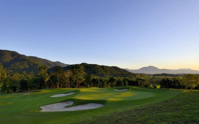 Scenic view of a golf course surrounded by lush green hills at Chiang Mai Highlands Golf and Spa Resort during sunset.