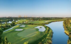 Aerial view of FLC Halong Bay Golf Club showcasing green fairways, sand bunkers, and a winding water feature surrounded by lush landscape under clear blue skies.
