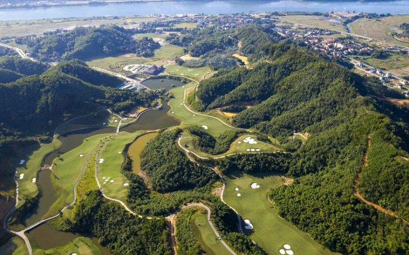 Aerial view of Hilltop Valley Golf Club, featuring a lush green golf course winding through rolling hills and valleys with scenic mountain landscapes in the background.