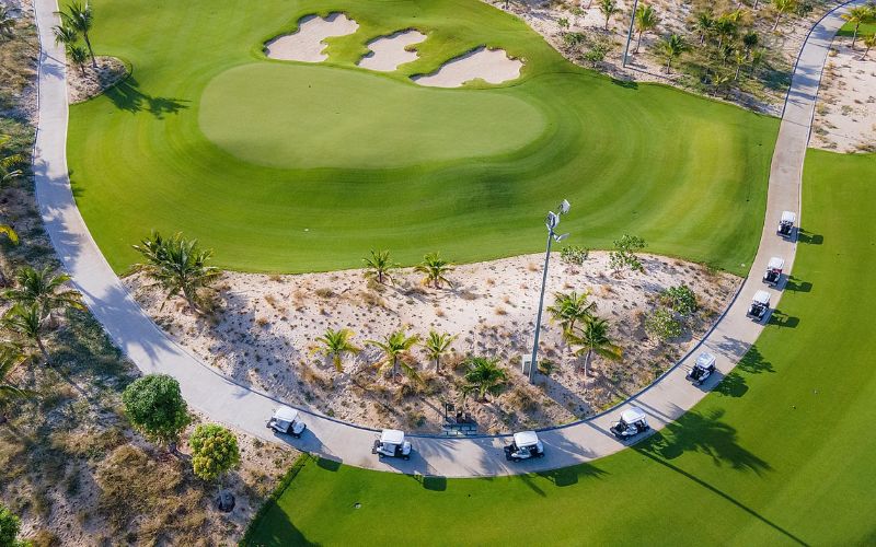 Aerial view of a green and surrounding bunkers at Hoiana Shores Golf Club, bordered by sandy terrain, pathways, and neatly maintained fairways.