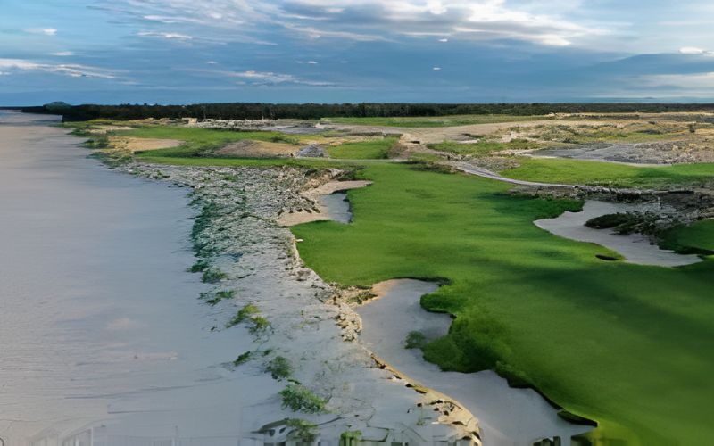 Scenic coastal view of Hoiana Shores Golf Club featuring lush green fairways running alongside a sandy beach and blue ocean under a partly cloudy sky.