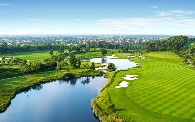 Scenic aerial view of Kings Island Golf in Hanoi, featuring lush green fairways, a lake, and surrounding natural landscape under a clear sky.