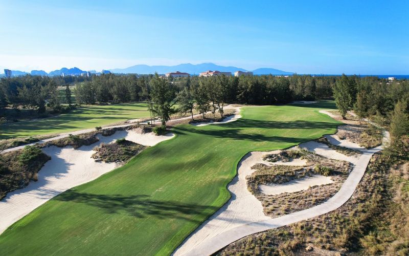Aerial view of the manicured fairways, sand bunkers, and surrounding trees at Kings Island Golf Resort under a clear blue sky.