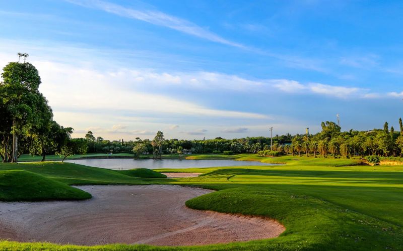 View of Laem Chabang International Country Club featuring a bright green fairway, sculpted bunkers, and a backdrop of trees under a clear blue sky.