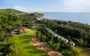 Aerial view of Laguna Lang Co Golf Club surrounded by lush greenery, mountains, and coastline, showcasing the scenic fairways and luxury resort area near the sea.