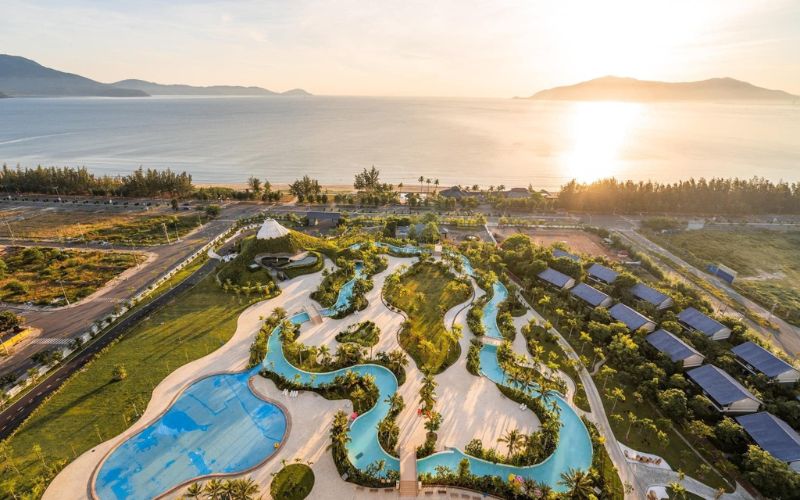 Aerial view of Mikazuki Japanese Resort & Spa featuring winding outdoor pools, landscaped gardens, and modern buildings set against a scenic coastal backdrop at sunset.