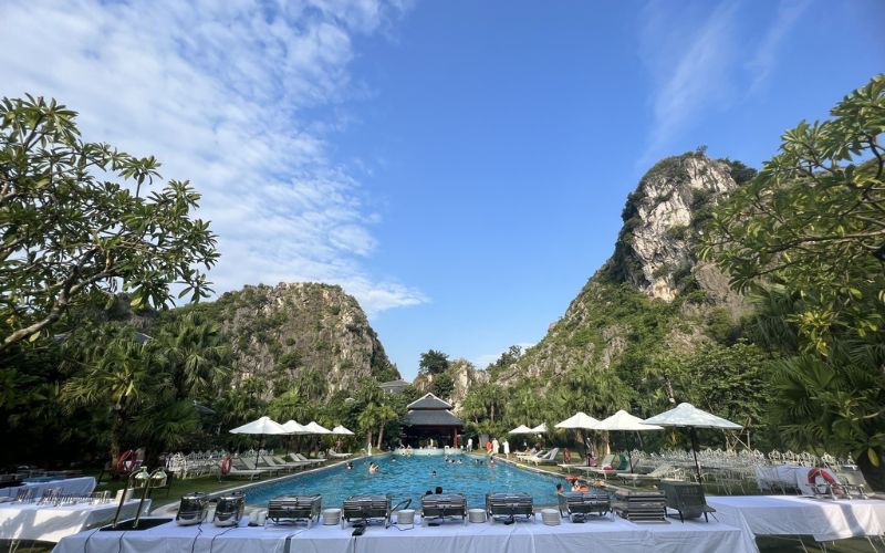 Poolside area at Minawa Kenh Ga Resort surrounded by trees and limestone mountains.