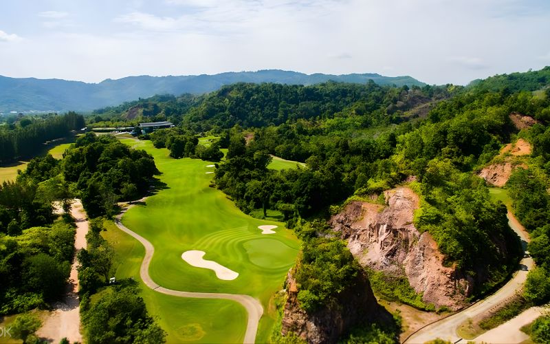 A scenic view of Red Mountain Golf Club with lush green fairways surrounded by rugged red cliffs and dense tropical forest.