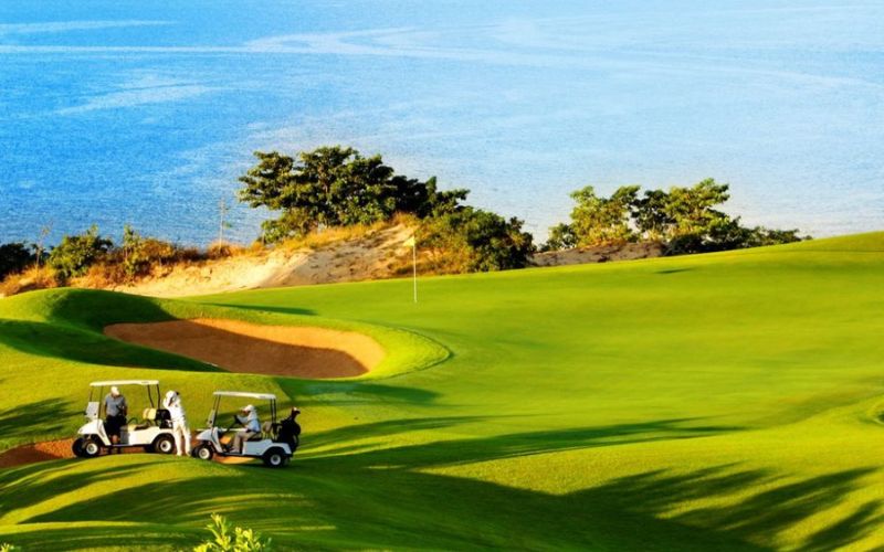 Scenic Sea Links golf course with a group of golfers riding in golf carts, set against a backdrop of green hills and trees.
