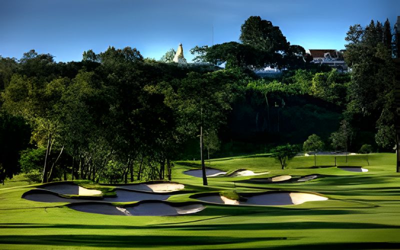 Beautiful fairway and greens at Siam Country Club, one of the luxury golf resorts in Thailand, surrounded by lush trees and rolling hills under a clear blue sky.