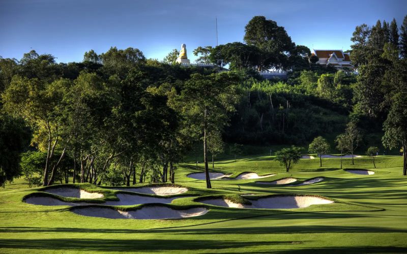 Scenic view of Siam Country Club in Pattaya featuring lush fairways, white sand bunkers, and surrounding hills under clear skies.