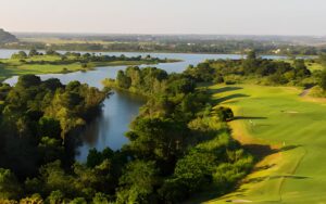 Aerial view of Sky Lake Golf Resort in Hanoi, featuring lush green fairways, a large lake, and surrounding natural landscapes under clear skies.