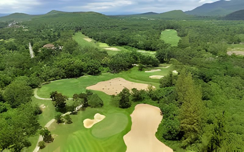 Aerial view of Springfield Royal Country Club surrounded by lush greenery, featuring rolling fairways, sand bunkers, and tree-lined holes set against distant hills under a clear sky.