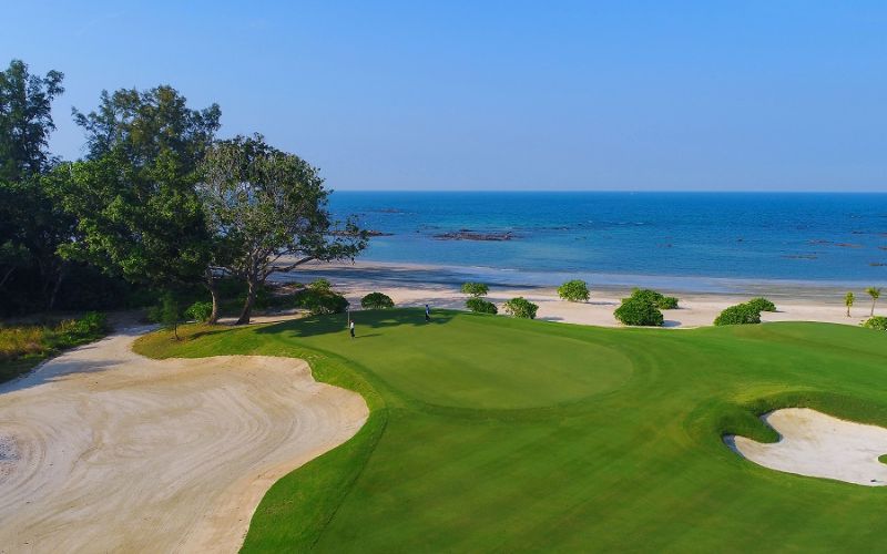 A bright aerial view of The Els Club Desaru Coast golf course with rolling fairways, water features, and sand bunkers spread across the landscape.