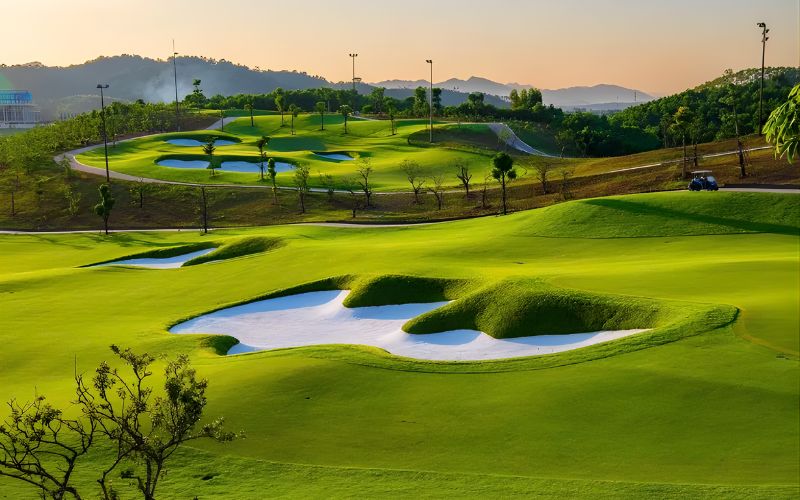 Wide view of Yen Bai Star Golf and Resort featuring bright green fairways, sculpted bunkers, rolling hills and a warm sunset glow over the landscape.