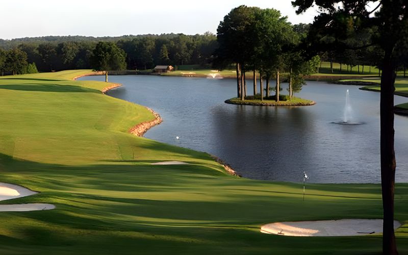 Pleasant Valley Golf Country Club with smooth fairways curving along a calm lake, surrounded by trees under clear sunlight.