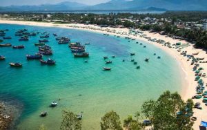 Aerial view of Quy Nhon coastal city with turquoise waters, sandy beach, and fishing boats along the bay.