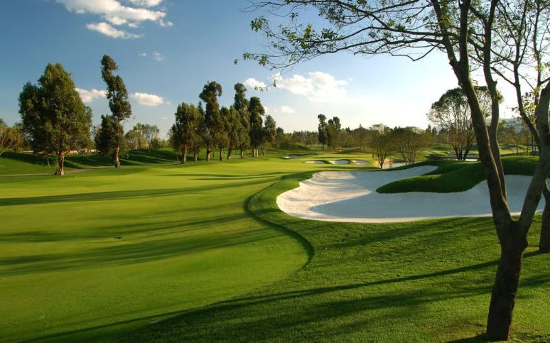 A golf hole at Kunming Lakeview Golf Club featuring a manicured fairway, white sand bunker, and mature trees under a partly cloudy sky.