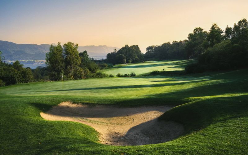 A scenic golf green at Spring City Golf and Lake Resort’s Mountainview Course, surrounded by rolling hills, lush fairways, and a large sand bunker at sunset.