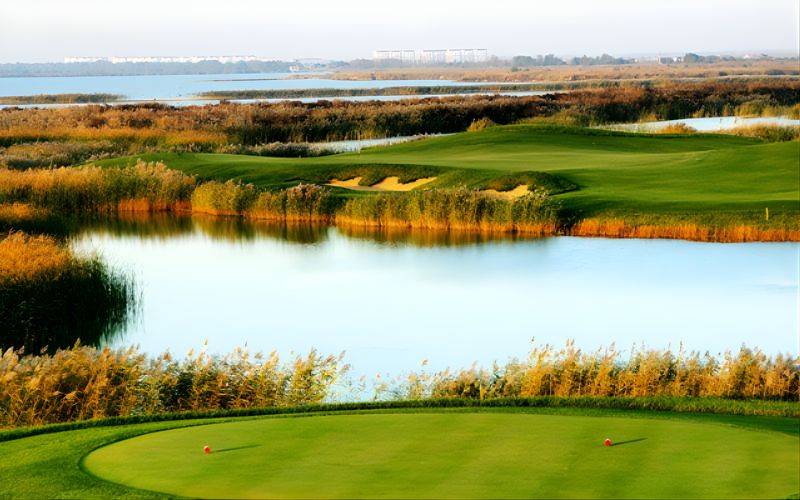 Caofeidian Wetlands International Golf Club course with a green set beside a calm lake, surrounded by natural reeds and wetland landscape.